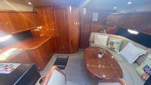 A compact, well-lit interior with a wooden kitchenette, a seating area with cushions, and a small table with a plant. - Boat Accommodation Ltd (Torquay)