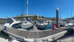 A marina with boats docked, a wooden pier, and a hill with buildings in the background. - Boat Accommodation Ltd (Torquay)