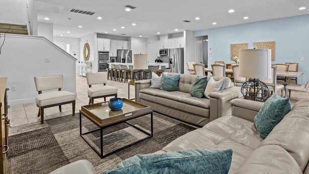 Een moderne woonkamer met een bank, stoelen, een salontafel en een keuken op de achtergrond.