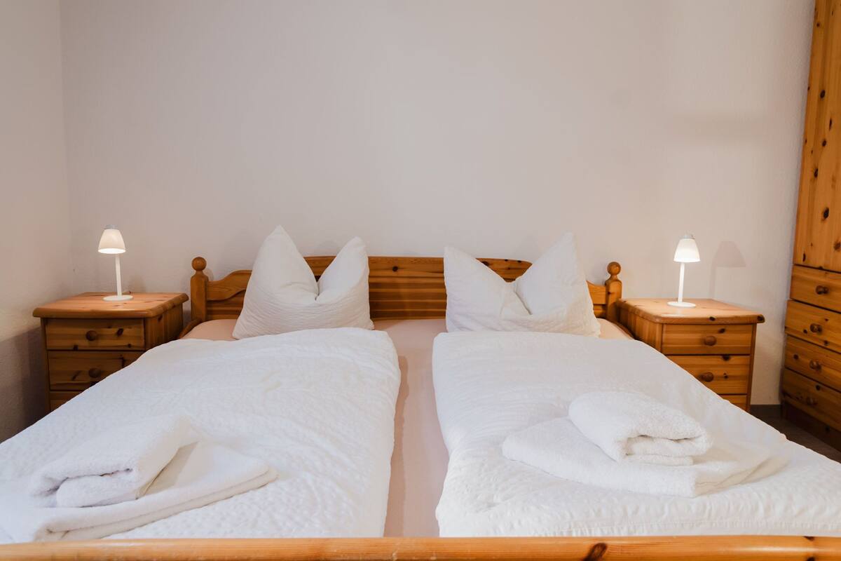 A double bed with white bedding, two bedside tables with lamps, and a wooden wardrobe.