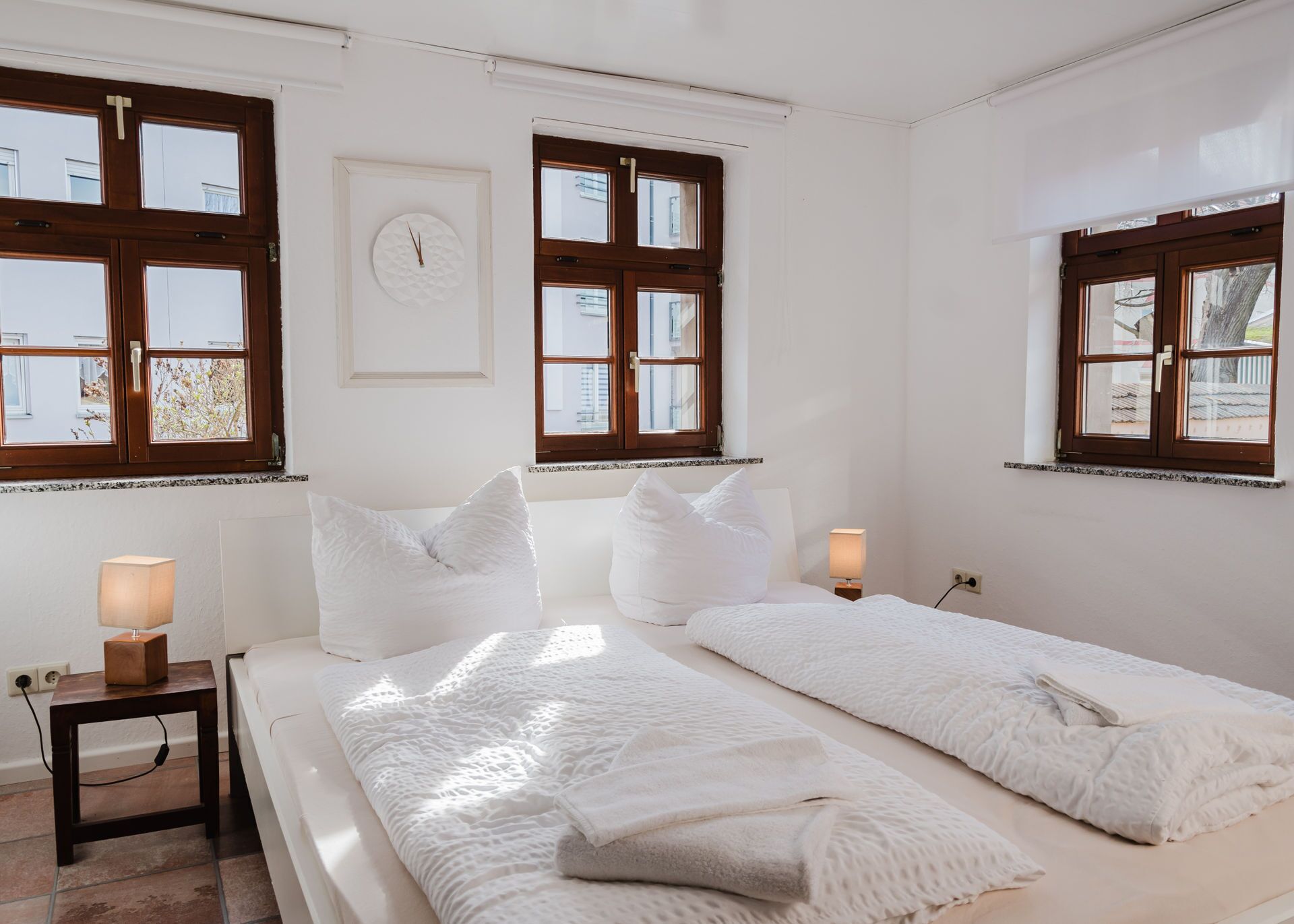 Ein Hotelzimmer mit zwei Betten, einem Nachttisch mit Lampe und einer Wanduhr.