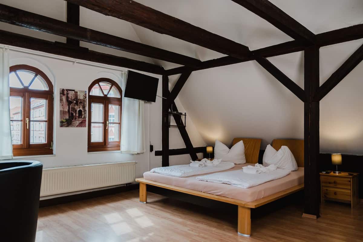 A bedroom with a wooden bed, white bedding, a TV mounted on the wall, and large windows with arched tops.
