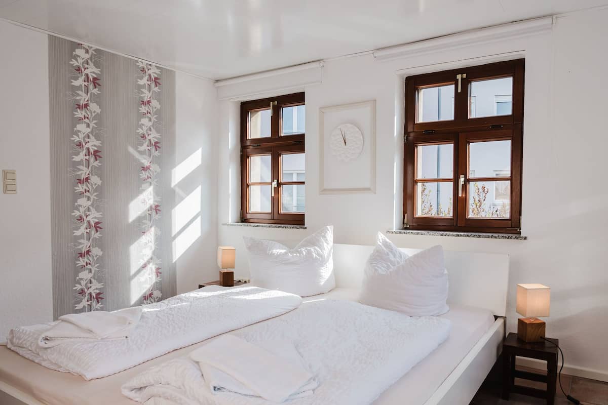 A hotel room with a large bed, two bedside tables, a window with a view, and a wall clock.