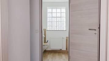 En smal gang, der fører til et badeværelse med et vindue, en radiator og et toilet.
