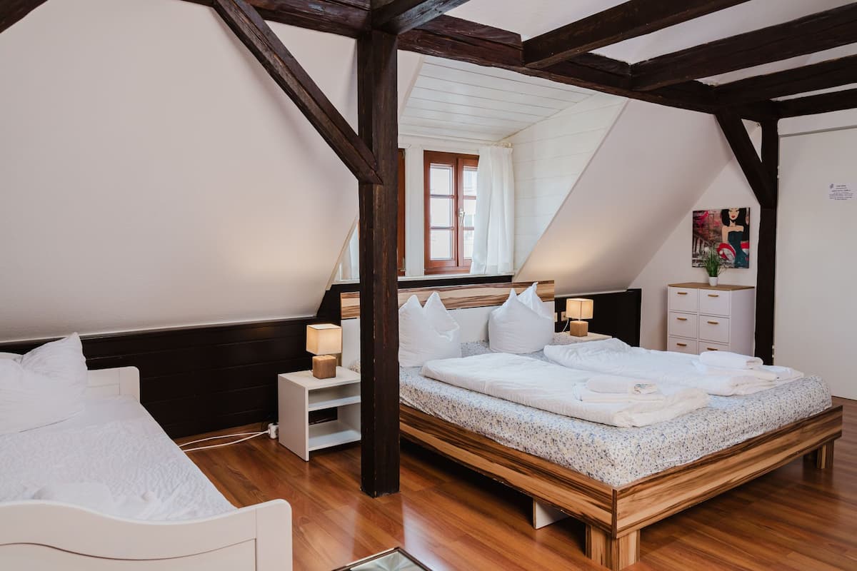 A bedroom with a wooden ceiling, a bed with white bedding, a nightstand, a dresser, and a window with curtains.
