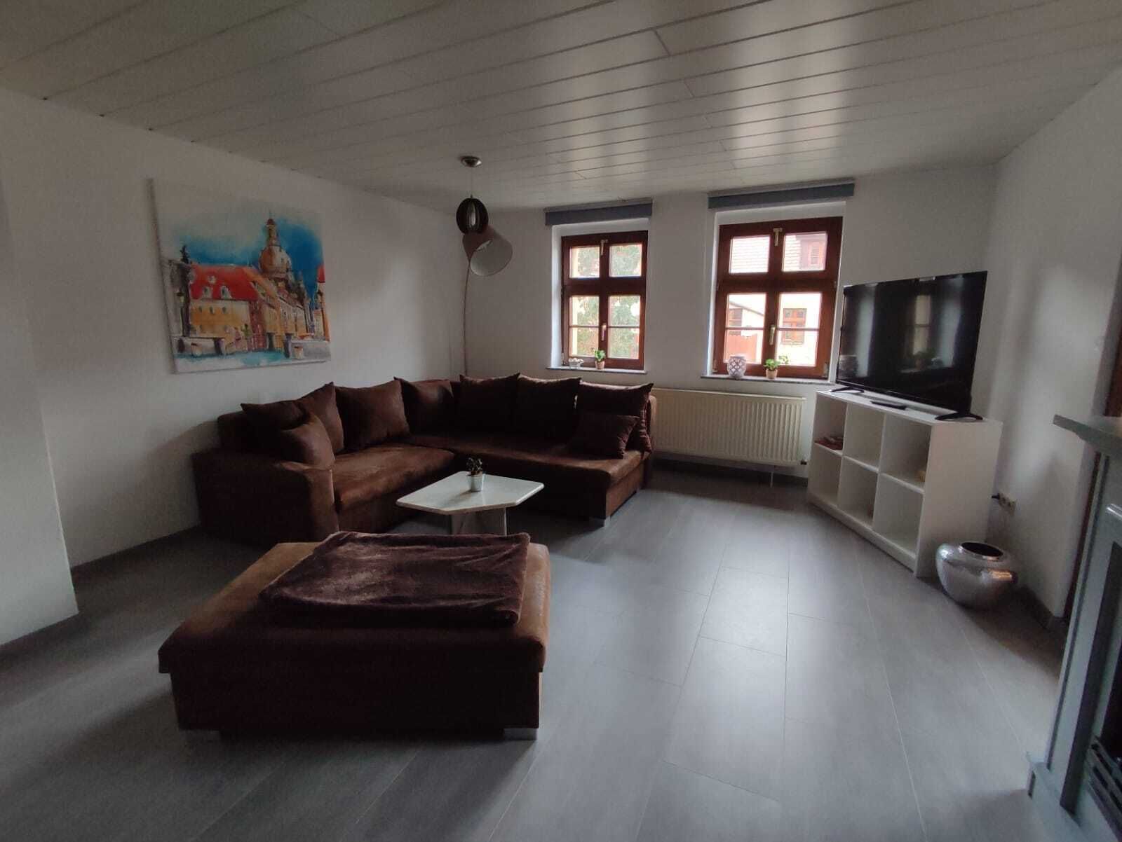 A living room with a brown sofa, a white coffee table, a television on a stand, and a painting on the wall.