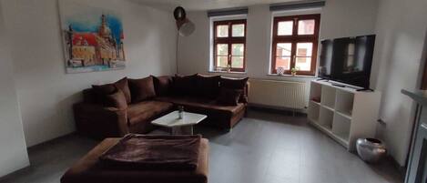 A living room with a brown sofa, a white coffee table, a television on a stand, and a painting on the wall.
