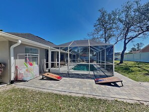 Relax on the covered patio, surrounded by a serene lawn and a tree, with a swimming pool nearby.