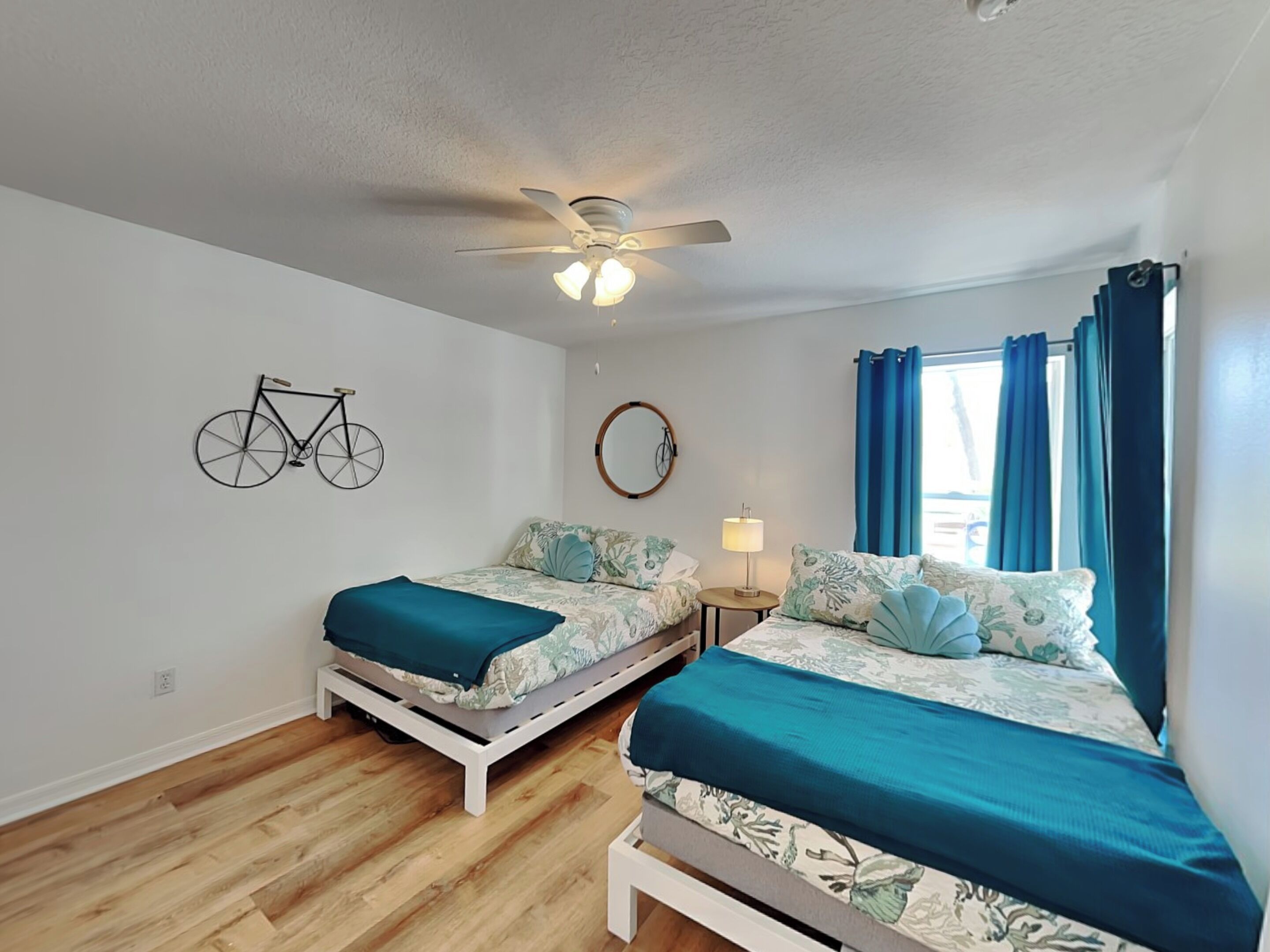 A bedroom with two beds, a ceiling fan, a bicycle on the wall, and a window with curtains.