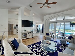 Relax in this stylish living area with a large flat-screen TV, ceiling fan, and expansive window offering a view of the outdoors.