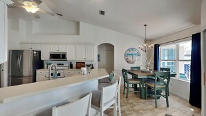 A modern kitchen with white cabinetry, a central island, and a dining area with green chairs. - Pet-Friendly Home with Private Pool, Fenced Yard + Near the Beach! (Palm Coast)