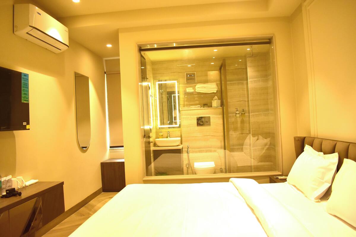 A hotel room with a bed, a bedside table, a mirror, a window, and a sliding glass door leading to a bathroom.