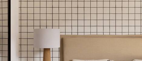 A bedroom with a grid-patterned wall, a bedside table with a lamp, a bed with pillows, and a bookshelf with books.