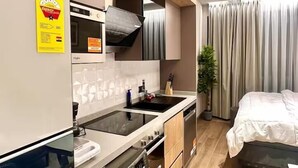 Una cocina moderna con horno empotrado, microondas y lavavajillas, junto a un dormitorio con cama grande y ventana.