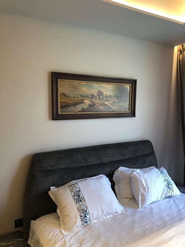 A hotel room with a bed, a headboard, a painting on the wall, and a curtain.