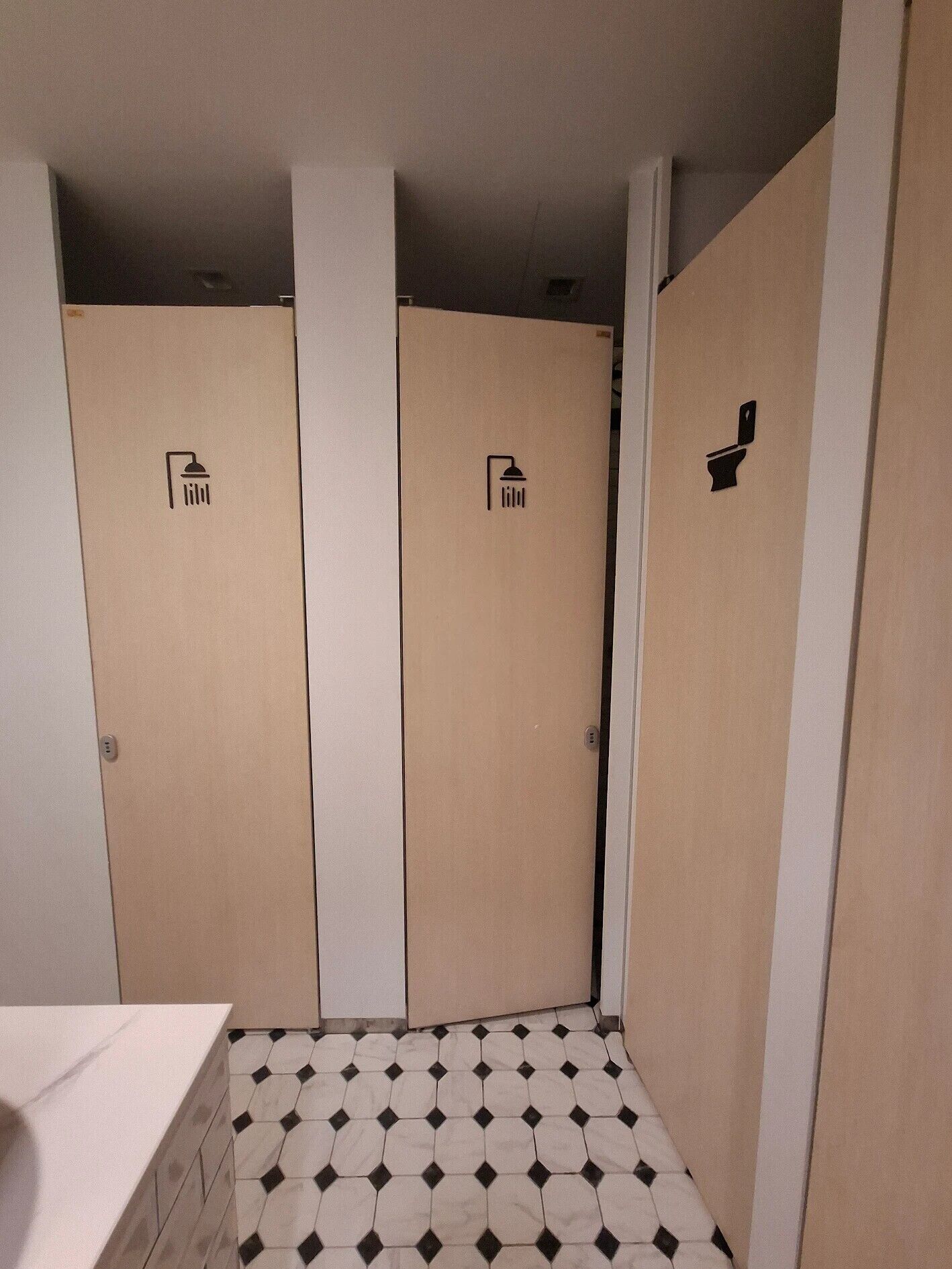 Un baño con tres cabinas, cada una señalizada con un icono de ducha e icono de inodoro en la pared.