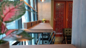 A dining area with a wooden table, chairs, and pendant lighting. There is a potted plant in the foreground. - N5 Ratchawong Hostel (Bangkok)