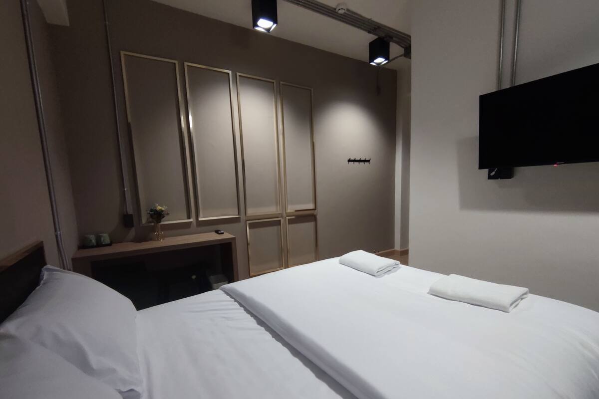Ett hotellrum med en säng, ett skrivbord med en lampa, en spegel och en tv som är monterad på väggen.