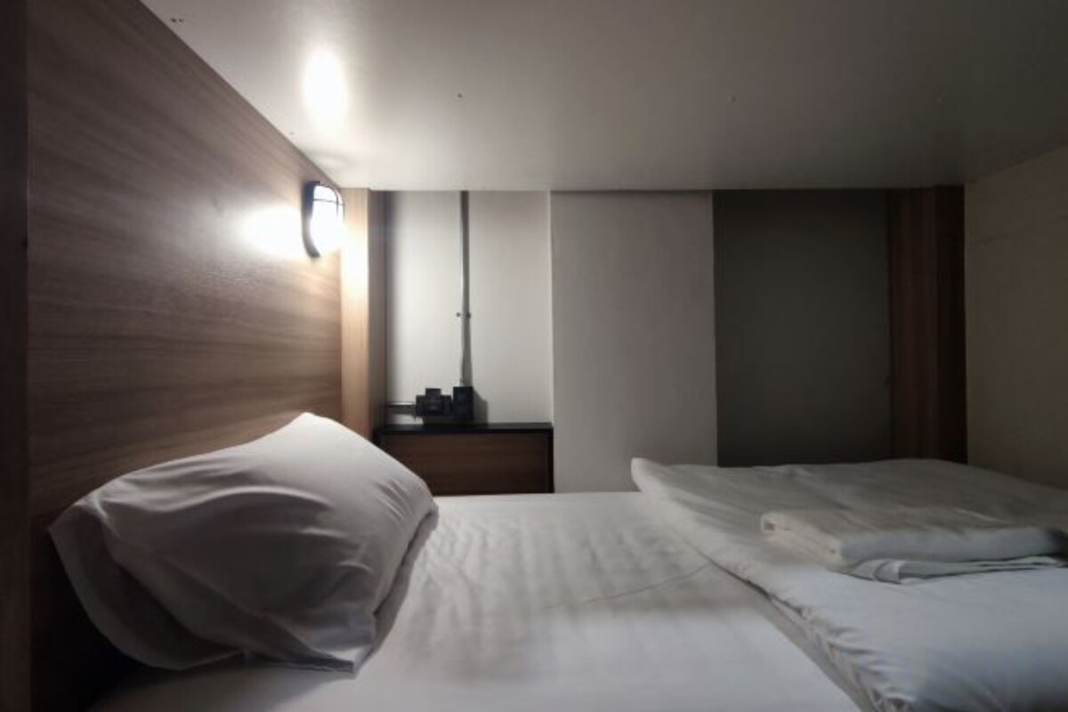 Ett hotellrum med en säng, ett nattduksbord, en spegel och en väggmonterad lampa.