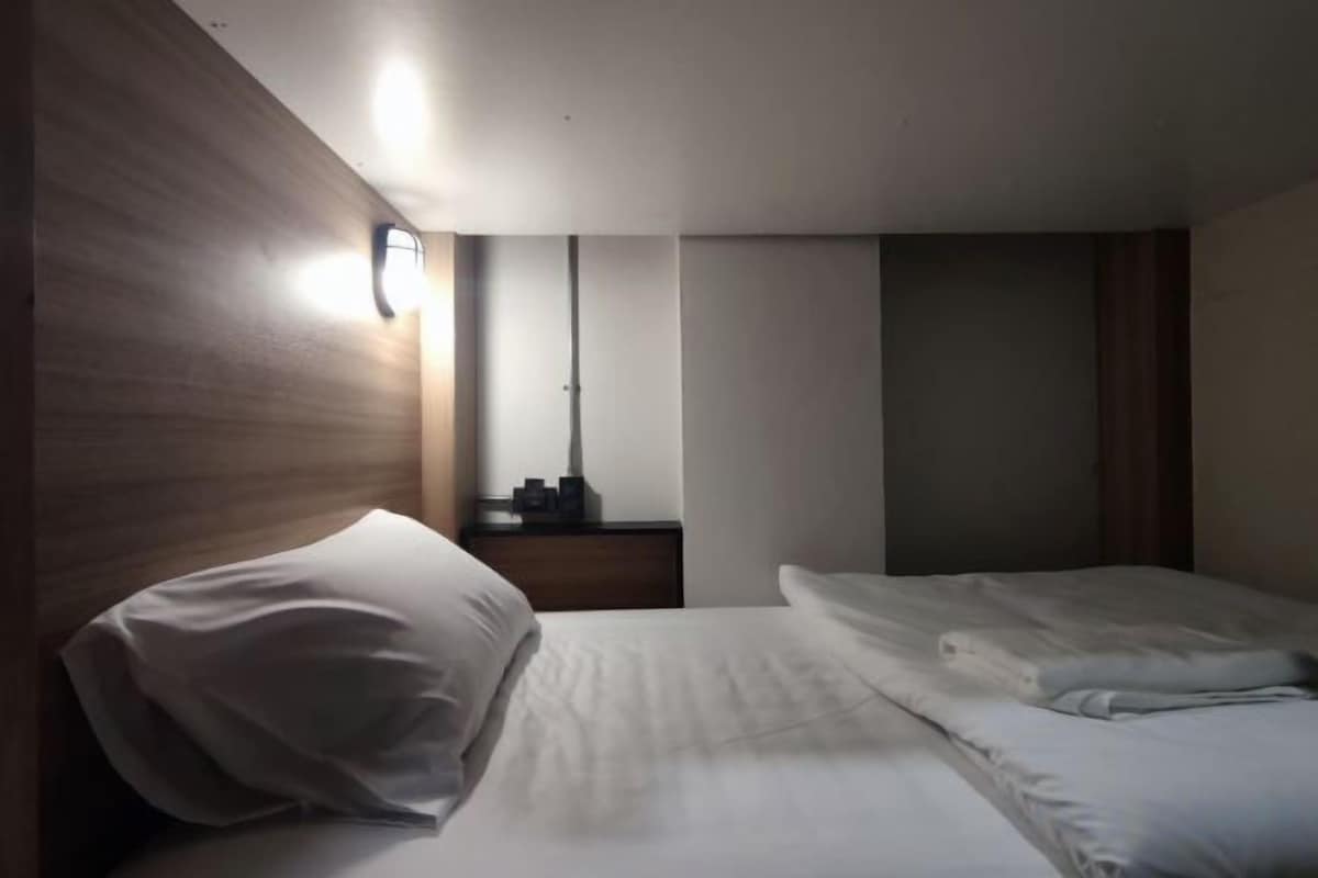 A hotel room with a bed, a nightstand, a mirror, and a wall-mounted light.