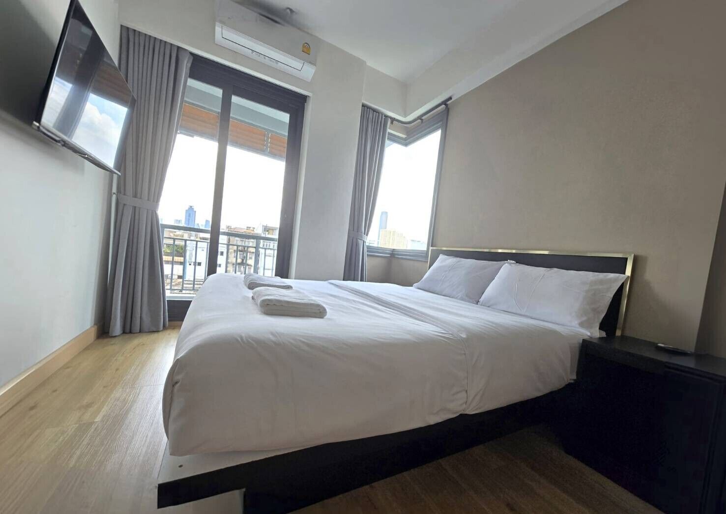 Habitación de hotel con cama, televisor de pantalla plana en la pared y ventana con cortinas.