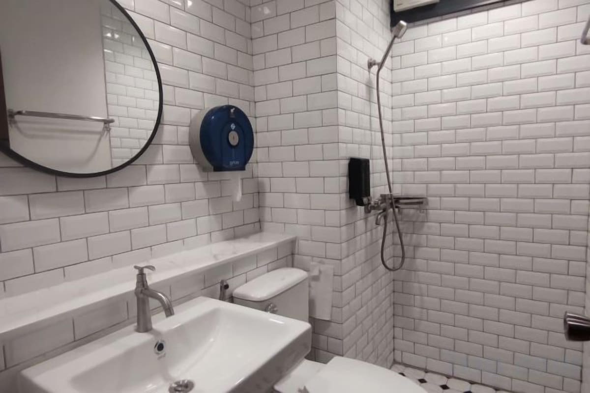 A bathroom with white tiled walls, a sink, a toilet, and a shower.