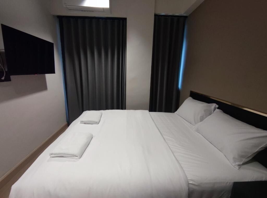 Ein Hotelzimmer mit einem Bett, zwei Kissen, einem flachbildfernseher an der Wand und einem fenster mit Vorhängen.