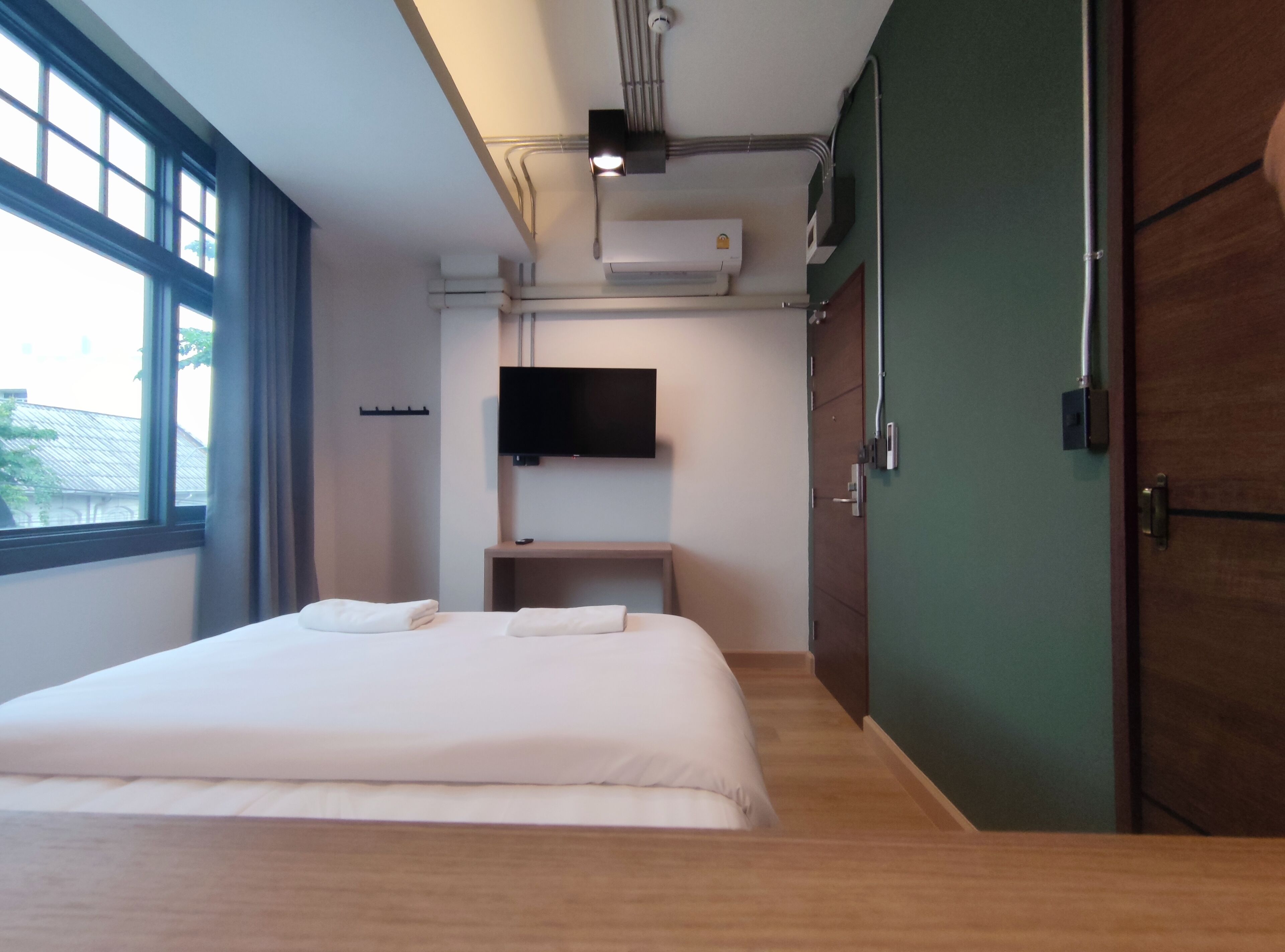 A modern hotel room with a large bed, a flat-screen TV mounted on the wall, and an air conditioning unit.