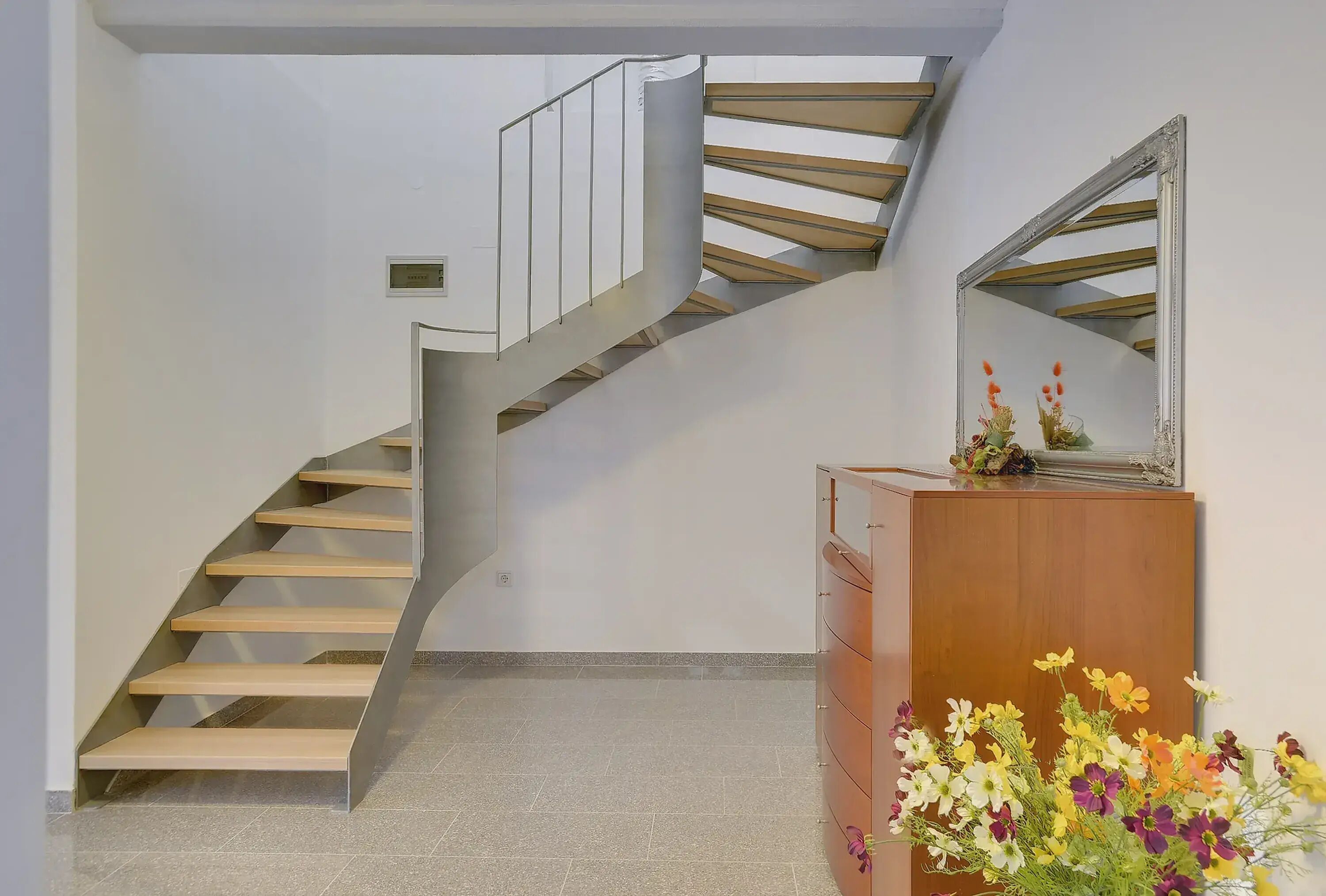 A modern interior with a spiral staircase, a wooden dresser, and a mirror.