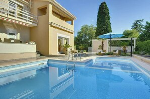A swimming pool with a metal ladder, a covered seating area, and a building with a balcony.