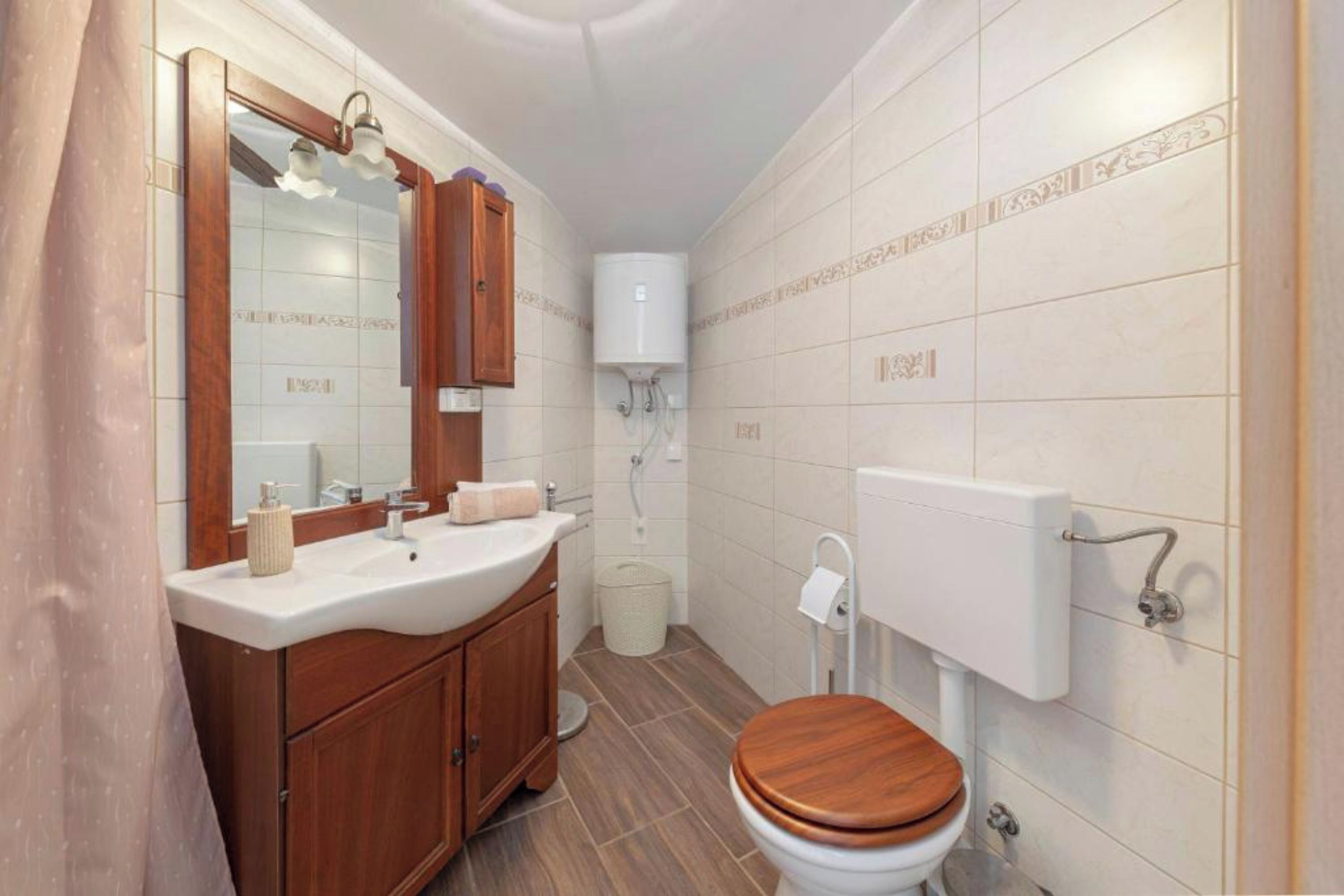 A compact bathroom with a wooden vanity, a white sink, a mirror, a toilet, and a shower area.