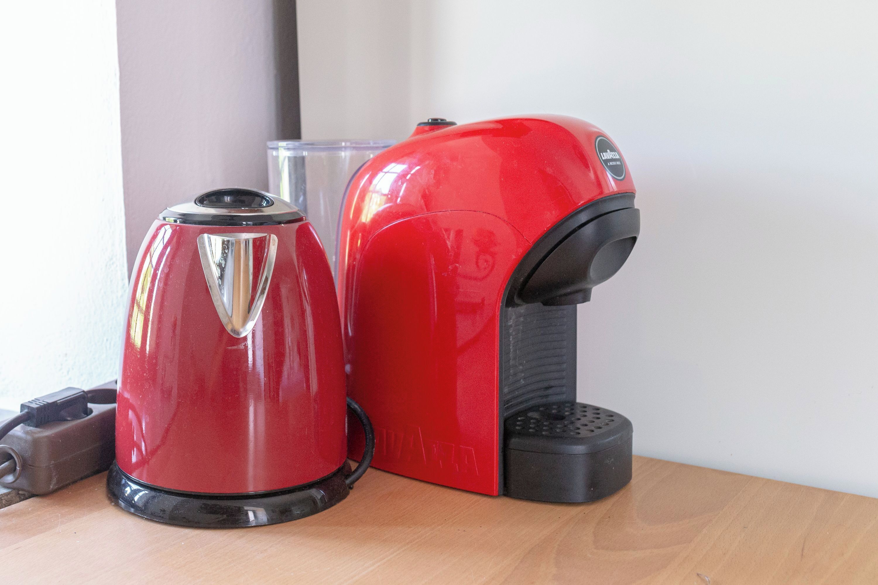 A red and black coffee maker on a wooden table next to a clear glass.