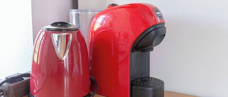 A red and black coffee maker on a wooden table next to a clear glass.