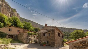 A stone building with a red-tiled roof, a small garden, and a mountainous backdrop. - Fairy-tale Tiny House From 17th Century (Koper)