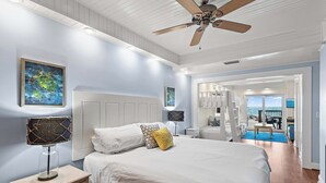 Un dormitorio con cama, mesitas de noche, ventilador de techo y obras de arte en las paredes.