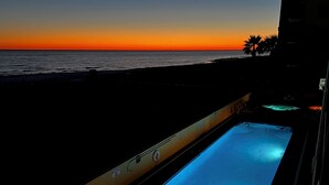 Une piscine avec vue sur le coucher de soleil, un panneau indiquant qu'il est interdit de se baigner et la silhouette d'un palmier.