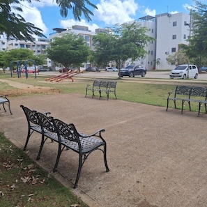 Stroll through the serene park area, featuring a paved walkway, benches, and a playground with a slide and swings.