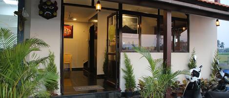 A building entrance with a welcome mat, potted plants, and a scooter parked outside.