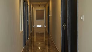 A long, narrow hallway with doors on both sides, recessed lighting, and a shiny floor. - Kings Residency (Tiruvannamalai)