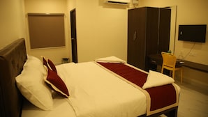 A hotel room with a bed, a desk, a chair, a wardrobe, and a TV. - Kings Residency (Tiruvannamalai)