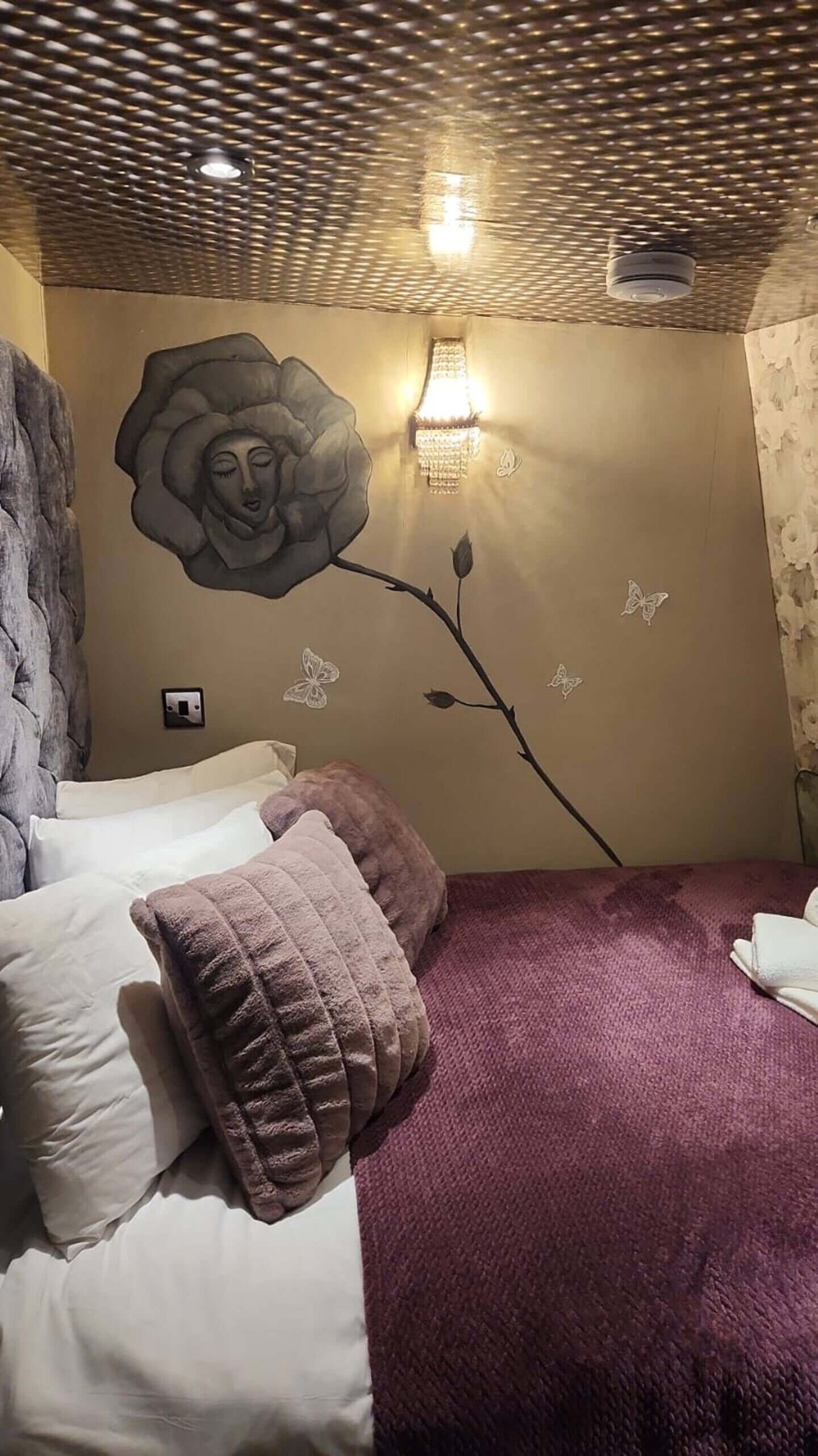 A bedroom with a bed, pillows, a wall mural, and a light fixture.