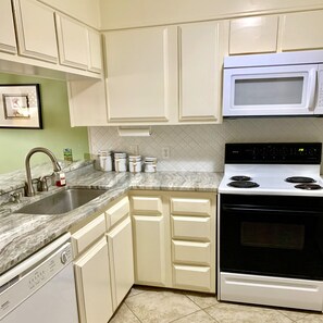 A kitchen with white cabinets, a stainless steel sink, a white microwave, and a black stove.