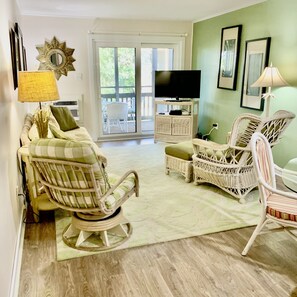 Sala de estar con muebles de mimbre, televisor y vistas al exterior.