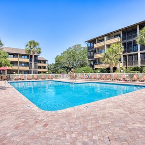 A swimming pool with lounge chairs and a building with balconies in the background.