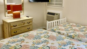 A bedroom with a bed, dresser, mirror, television, and air conditioning unit.