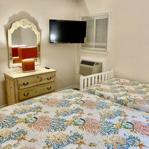 A bedroom with a bed, dresser, mirror, television, and air conditioning unit.
