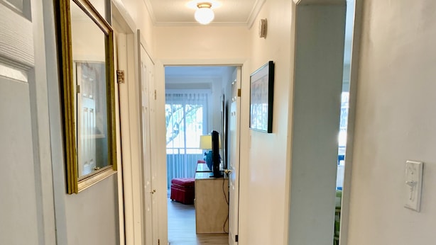 A hallway with a wooden floor, white walls, and a door on the left.