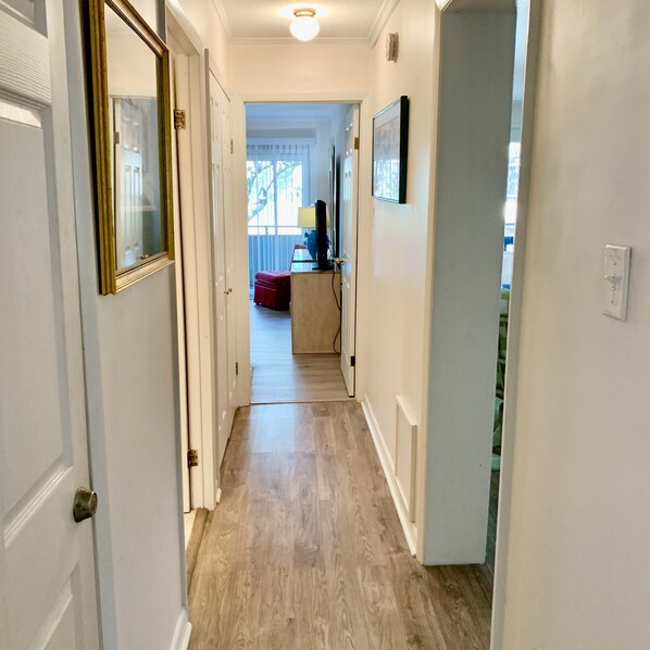 A hallway with a wooden floor, white walls, and a door on the left.