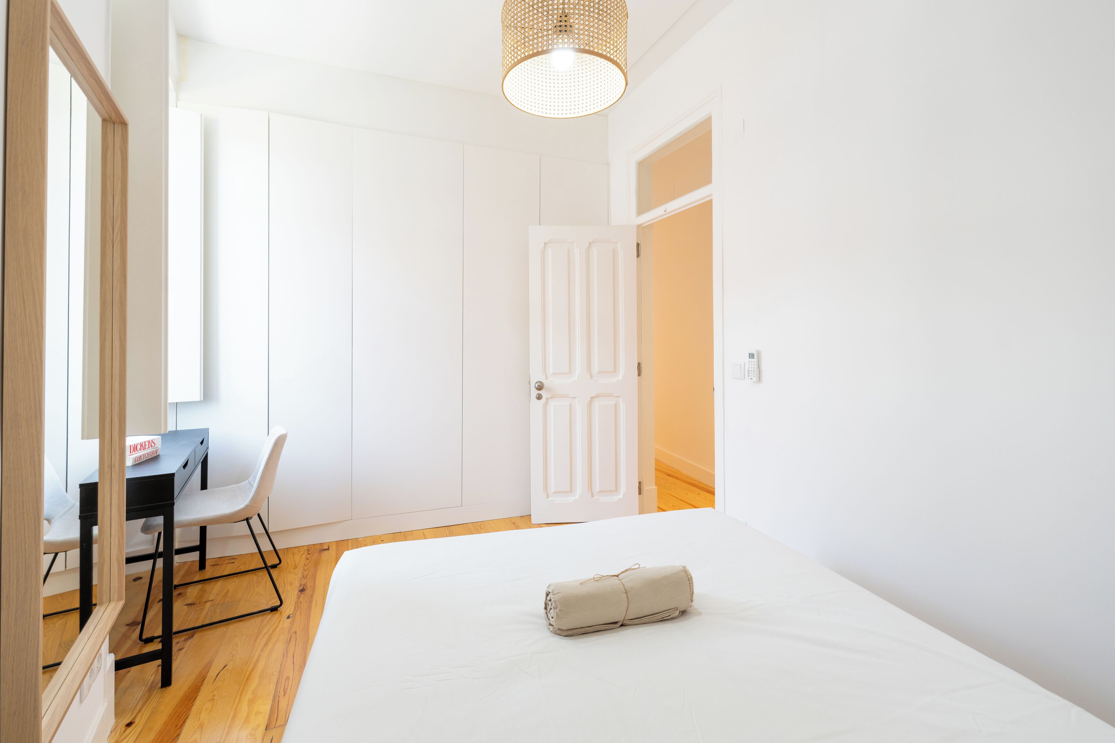 A bedroom with a bed, a desk with a chair, a wardrobe, and a door.