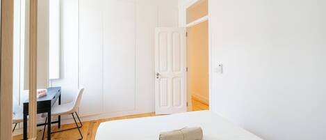 A bedroom with a bed, a desk with a chair, a wardrobe, and a door.